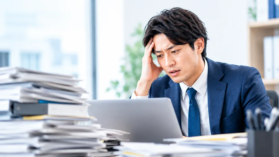 山積みの物件資料を前に、ひとりで頭を抱える様子